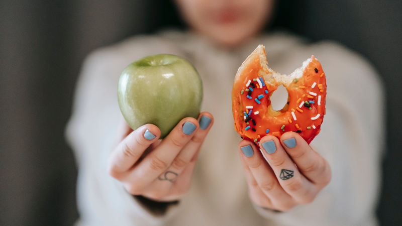 Девушка держит яблоко и пончик